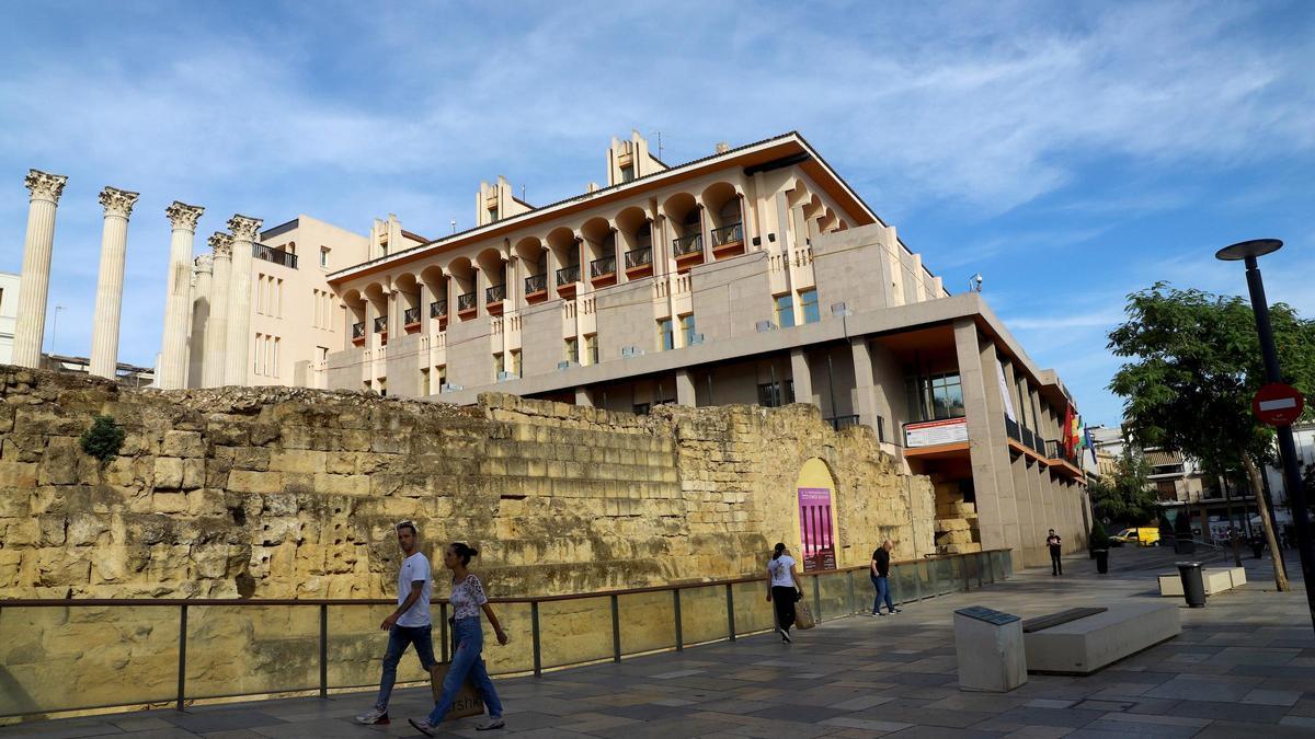 Varias personas pasean por delante del Templo Romano con la fachada del Ayuntamiento de Córdoba al fondo.