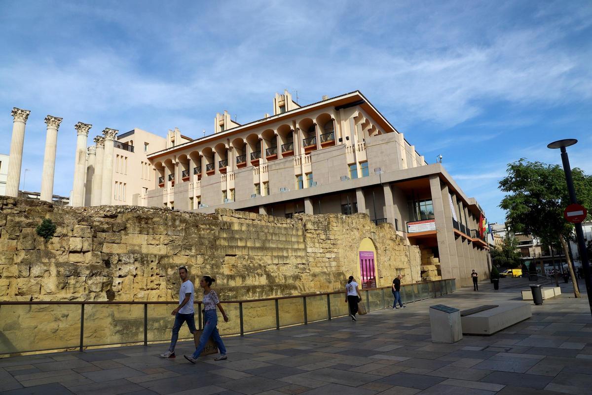 Varias personas pasean por delante del Templo Romano con la fachada del Ayuntamiento de Córdoba al fondo.