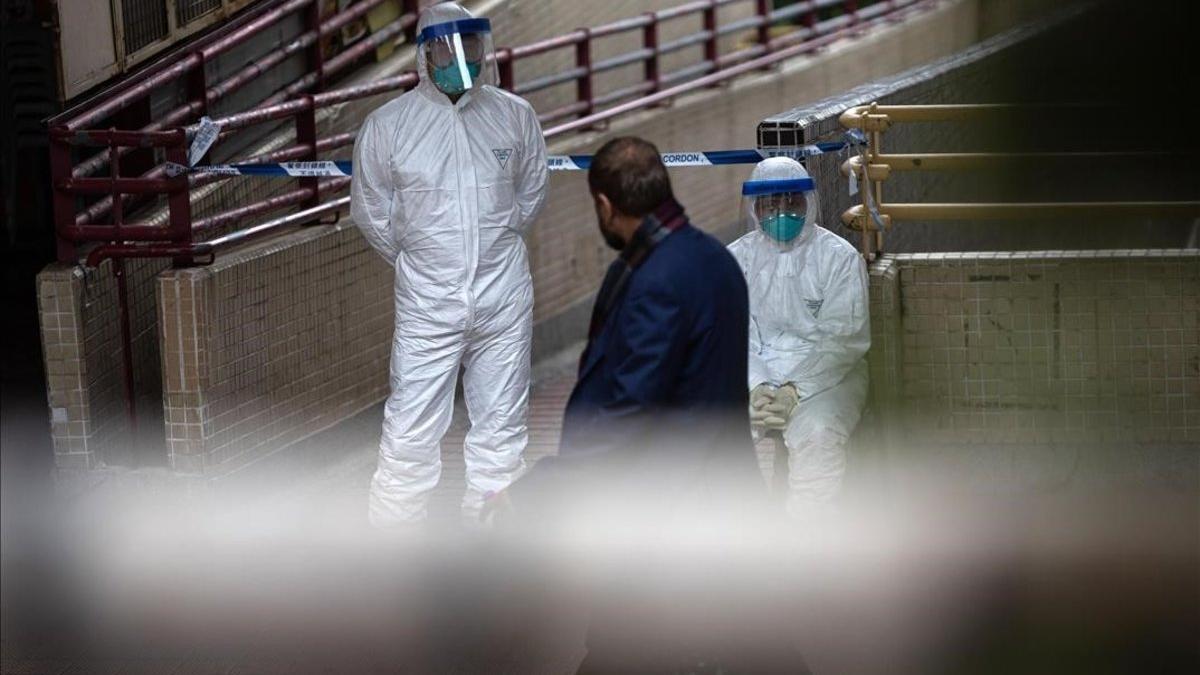 Un residente en Hong Kong pasa delante de unos policías, todos protegidos frente al coronavirus