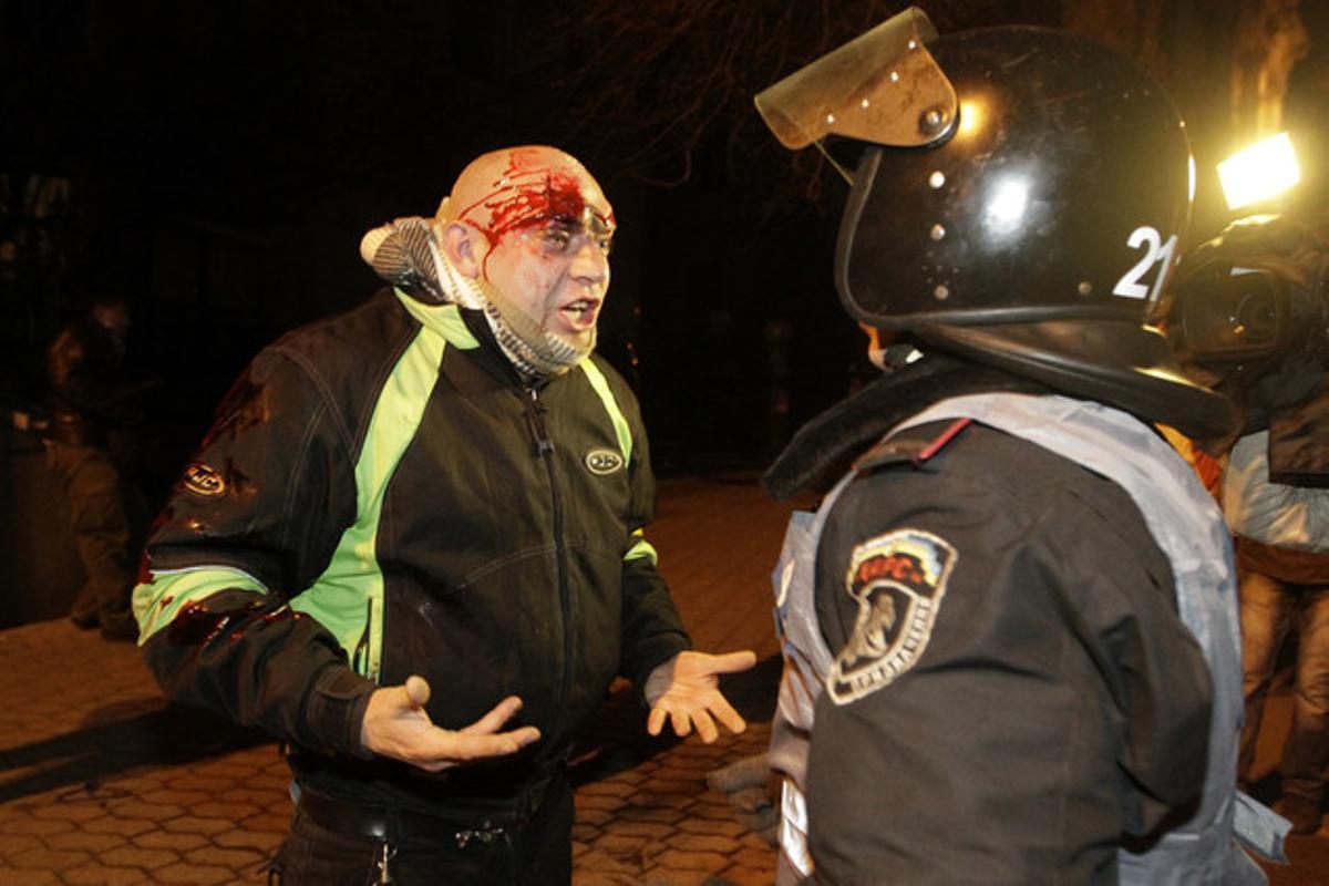 Un manifestante con una herida en la cabeza protesta frente un policía.