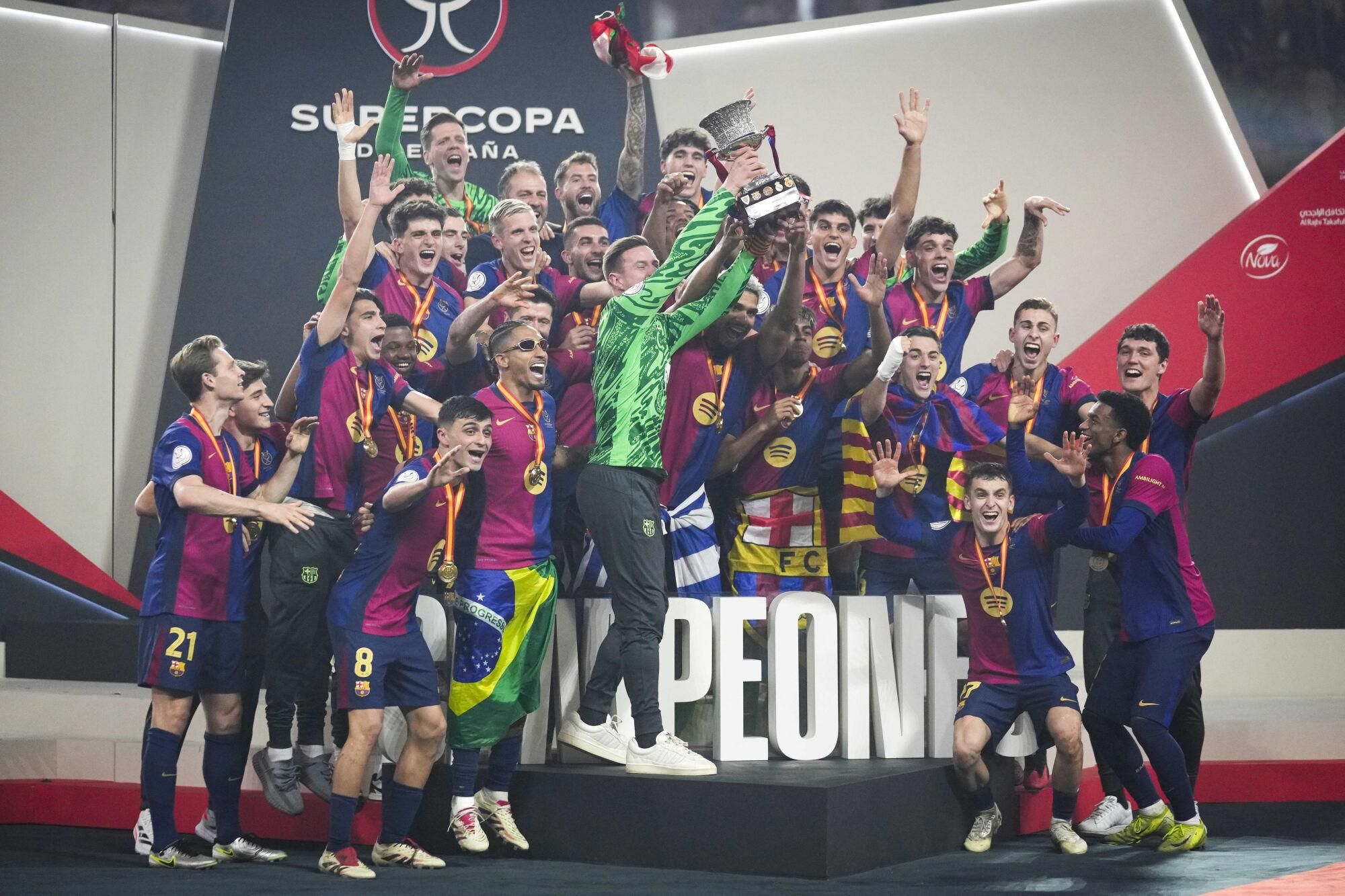 Barcelona players celebrate with their team's trophy of the Spanish Super Cup after the final soccer match between Real Madrid and Barcelona at King Abdullah Stadium in Jeddah, Saudi Arabia, Monday, Jan. 13, 2025. (AP Photo/Altaf Qadri). EDITORIAL USE ONLY/ONLY ITALY AND SPAIN