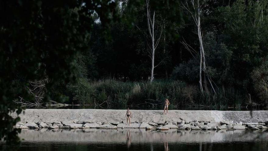 Dos jóvenes se disponen a bañarse en el Duero, donde el caudal ya está tan bajo que no cubre el azud.