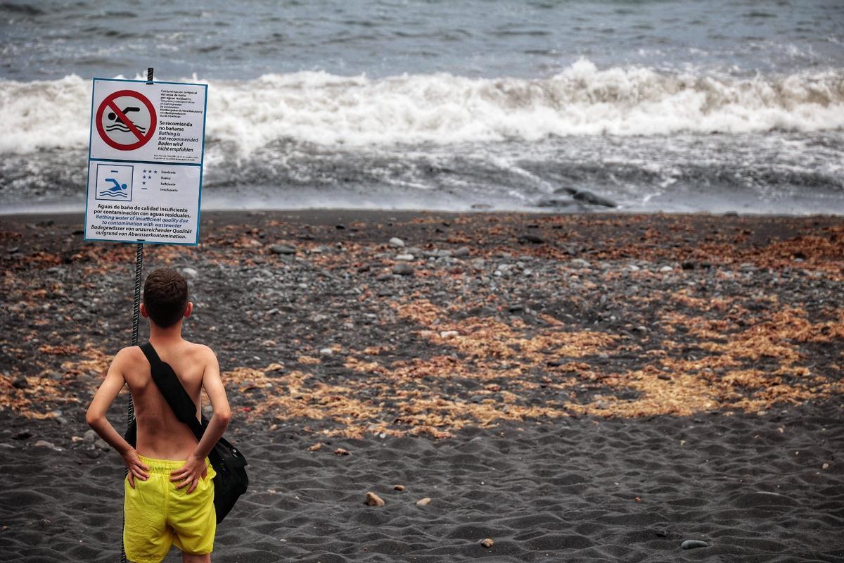 Un joven observando un cartel que indicaba el cierre de Playa Jardín, en Puerto de la Cruz