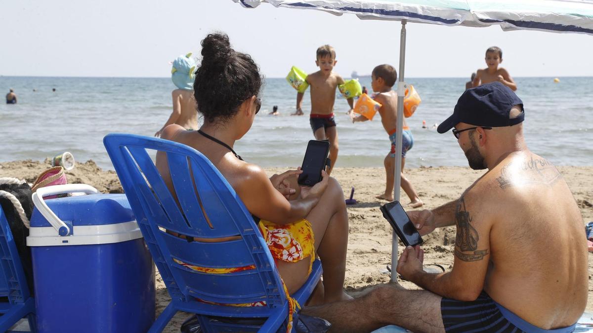 Dos personas consultan su teléfono móvil en la playa.