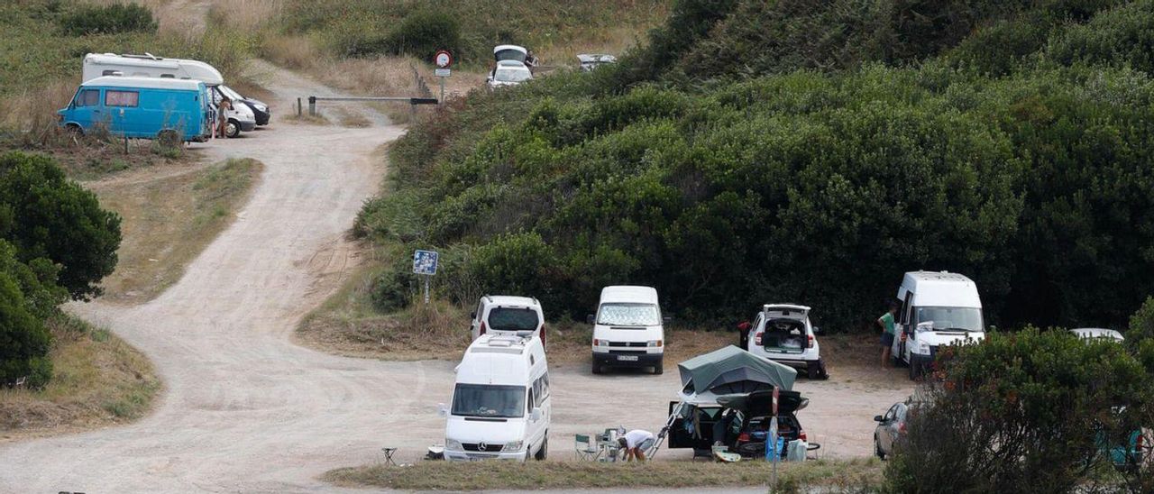 Junto a estas líneas, el parking de Xagó, con las autocaravanas estacionadas casi a pie de playa. Arriba, bañistas y surfistas en una jornada soleada en el arenal. | MARA VILLAMUZA / M. F.