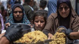 Palestinos desplazados sostienen ollas y sartenes de metal mientras se reúnen para recibir comidas calientes de un comedor social en el norte de la ciudad de Gaza,.