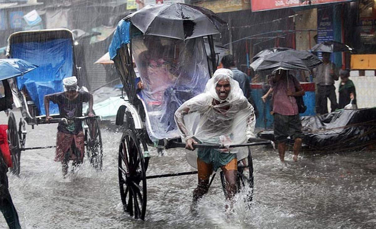Uns conductors de ’ricksaws’ treballen sota la pluja transportant passatgers pels carrers de Calcuta, inundats per les pluges del monsó, que va arribar a l’Índia a finals de maig.