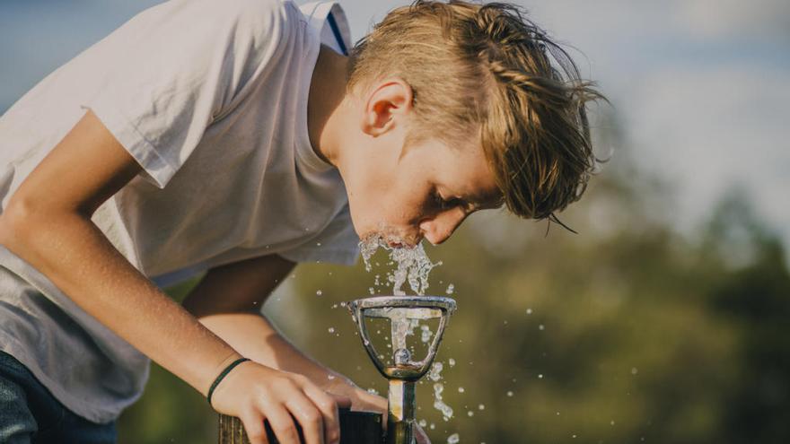 Un joven bebe agua de una fuente.