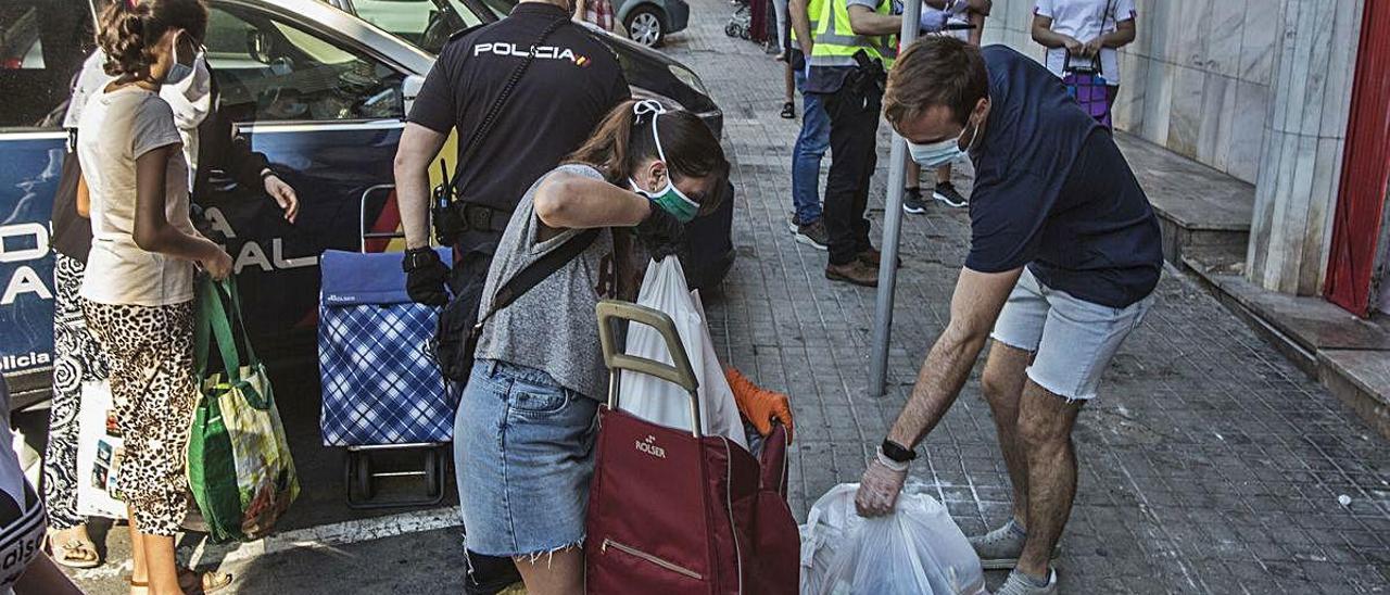 Varias personas recogen alimentos de una despensa solidaria.