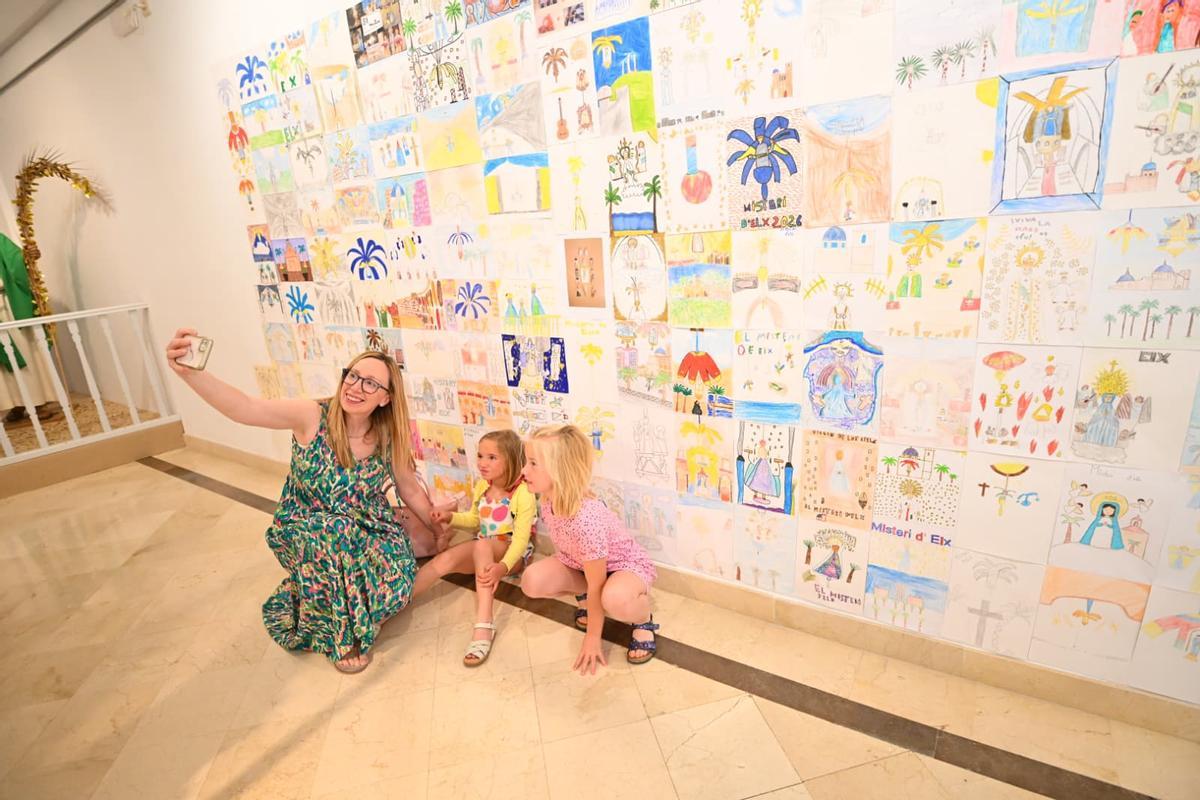 Familia posando ante una de las paredes de la exposición de dibujos infantiles.