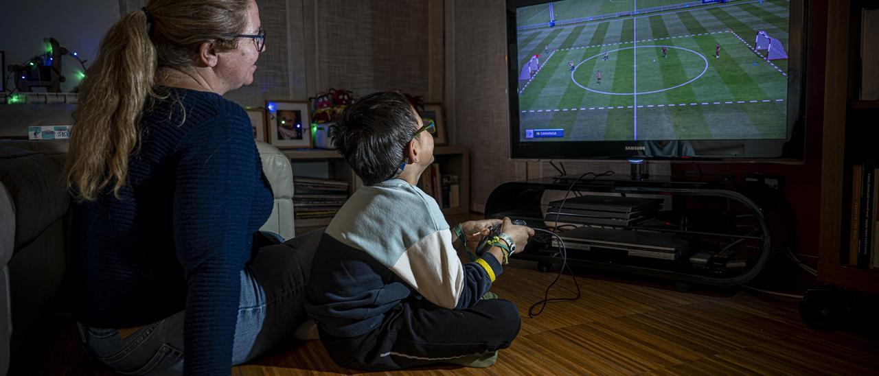 Un madre juega con su hijo a un videojuego de fútbol en su casa, en Barcelona.