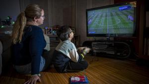 Un madre juega con su hijo a un videojuego de fútbol en su casa, en Barcelona.