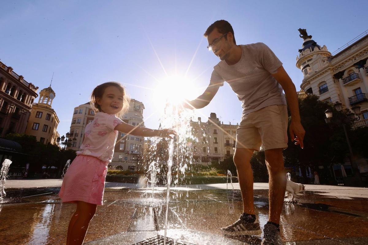Un hombre juega con su hija en la fuente de Las Tendillas.