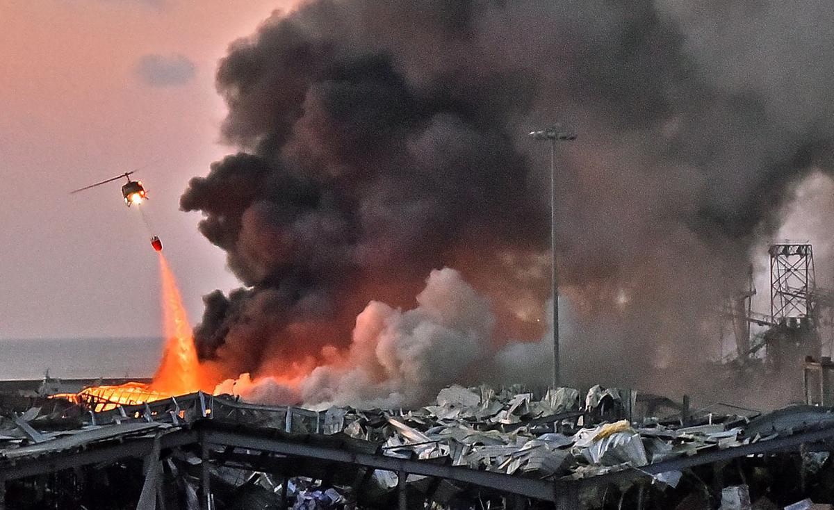 Imagen del 4 de agosto de 2020, un helicóptero apaga un incendio en la escena de una explosión en el puerto de la capital del Líbano, Beirut. - Líbano, golpeado por la crisis, cumple dos años el 4 de agosto de 2022 desde que una explosión masiva lo arrasó