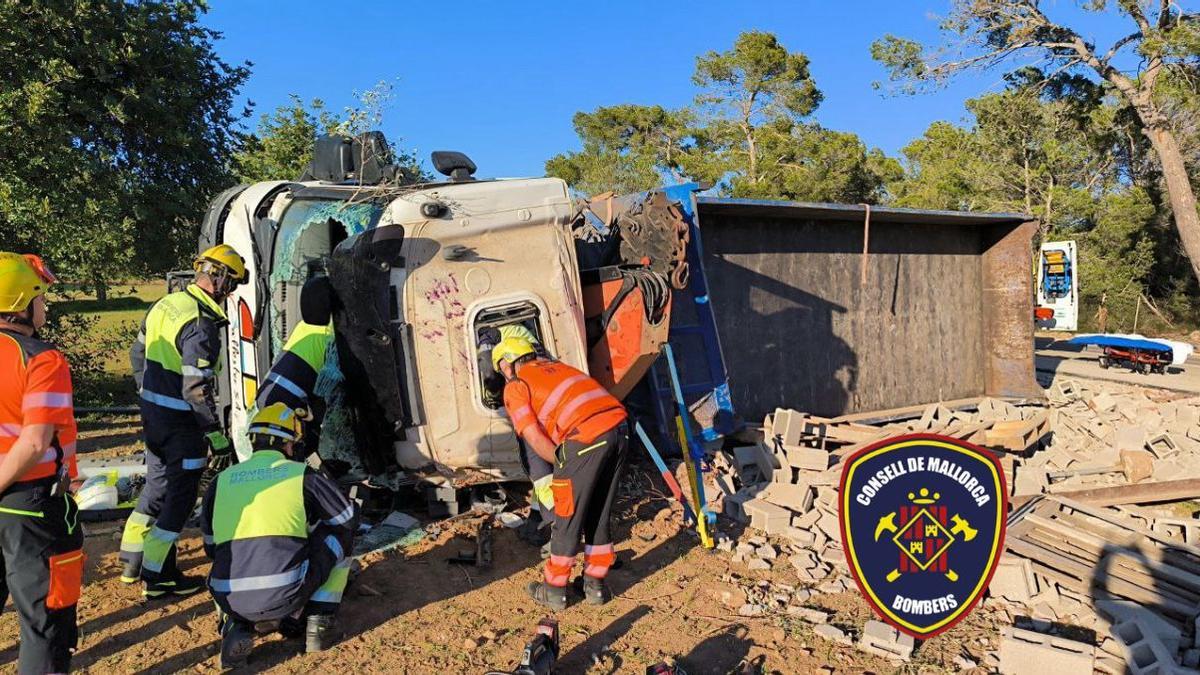 Bombers de Mallorca y personal sanitario tratan de atender al camionero atrapado en el interior tras volcar el vehículo.