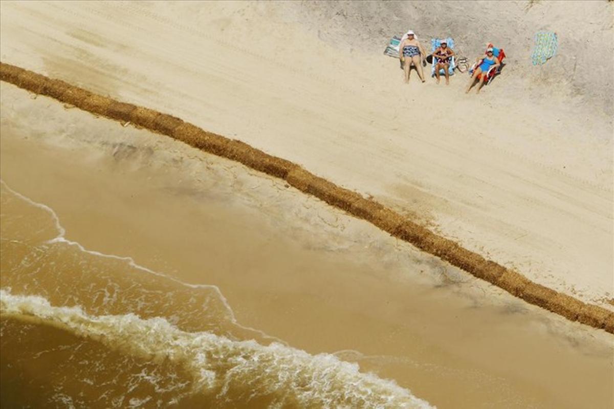 Beach goers sunbathe behind a wall of hay bales, used to absorb any oil that might come ashore, on Dauphin Island, Alabama in this May 11, 2010 file photo.