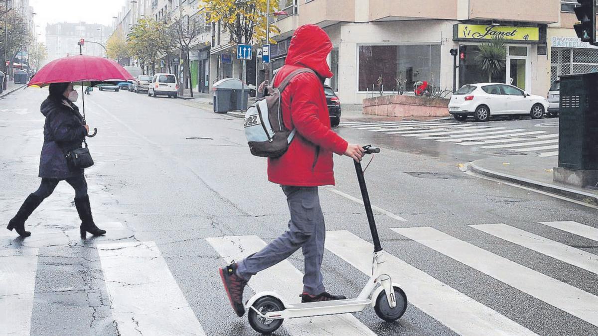 Un joven lleva de la mano un patinete eléctrico al cruzar un paso de peatones en Vigo