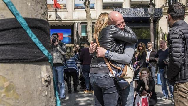 Varias personas lloran tras depositar flores en el lugar en el que fue asesinado un policia durante un ataque yihadista perpetrado en la avenida de los Campos Eliseos de París.