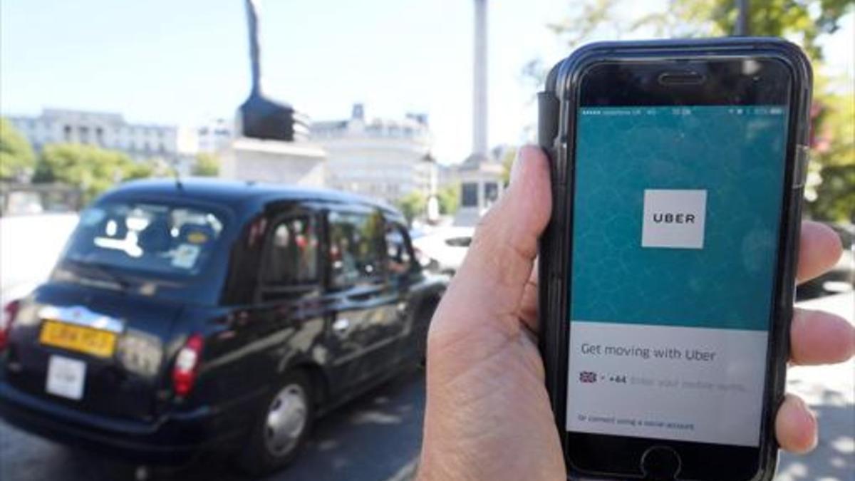 Un taxi de Londres pasa delante de un móvil con la aplicación de Uber activada, ayer.