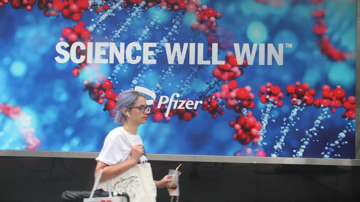 Una mujer camina junto a un cartel de la farmacéutica Pfizer.