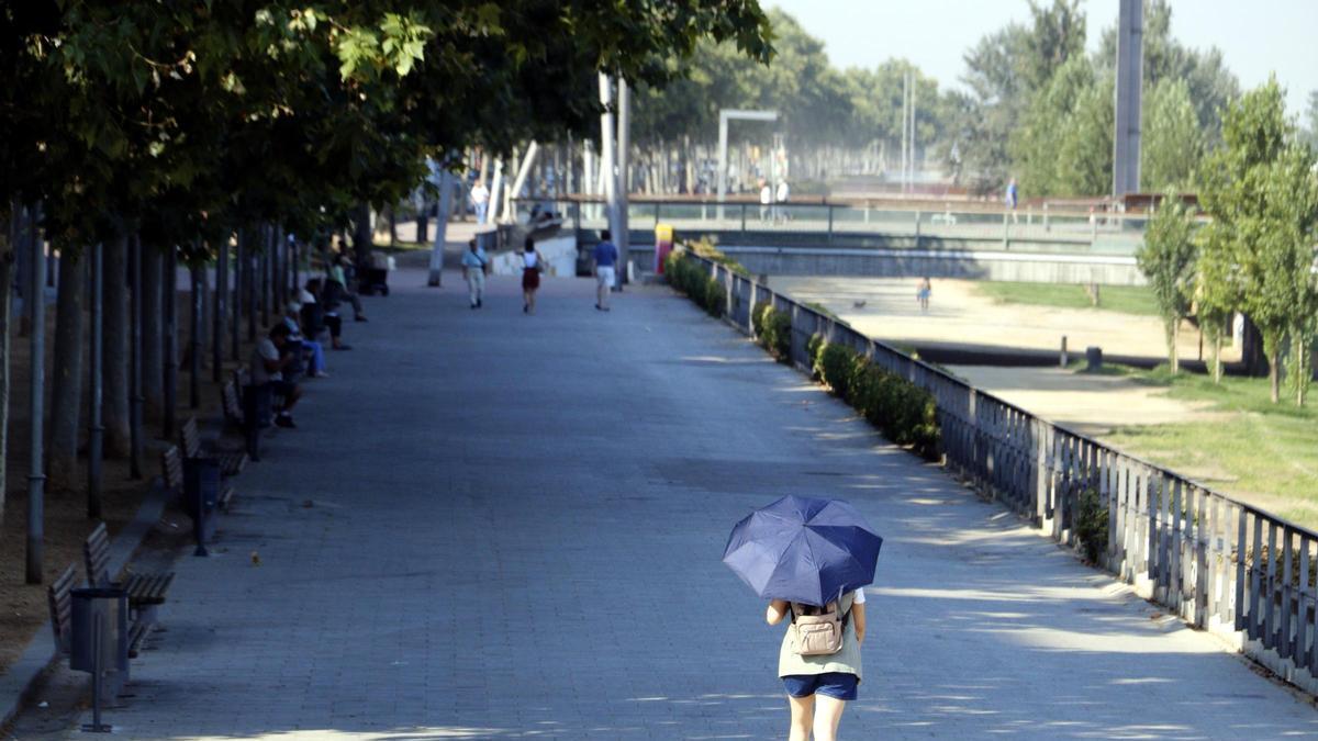Una dona camina amb un paraigua pel carrer Jaume II de Lleida, vora la canalització del riu Segre, durant l'onada de calor