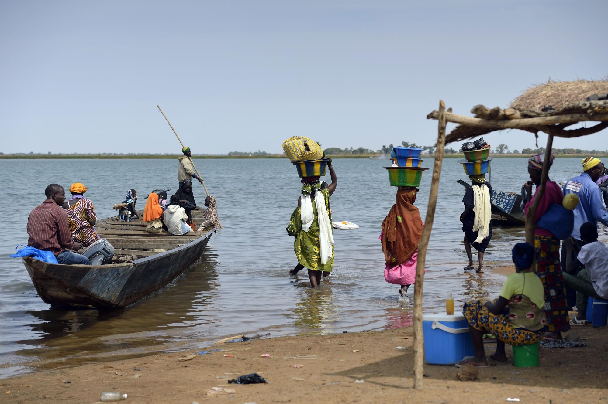 Un grupo de gente en la orilla del río Níger junto con una embarcación de madera.