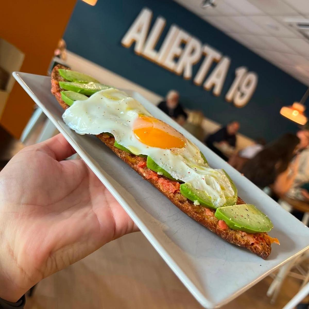 Una tostada con tomate rallado, aguacate y huevo frito