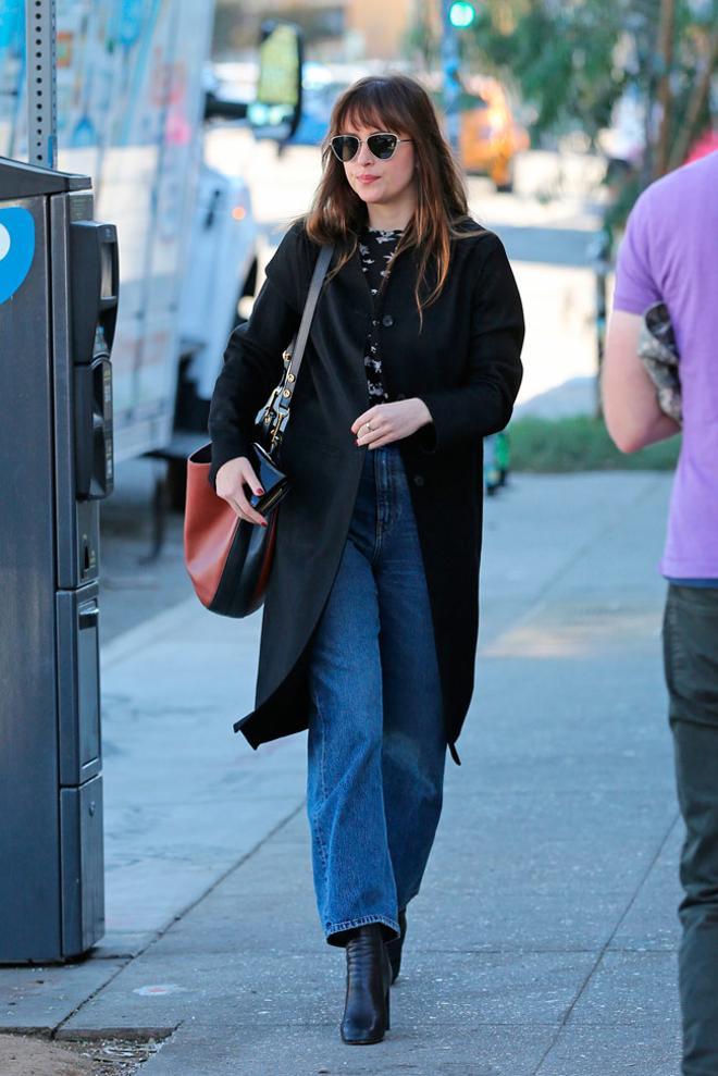 Dakota Johnson con vaqueros rectos, abrigo negro y bolso de Celine