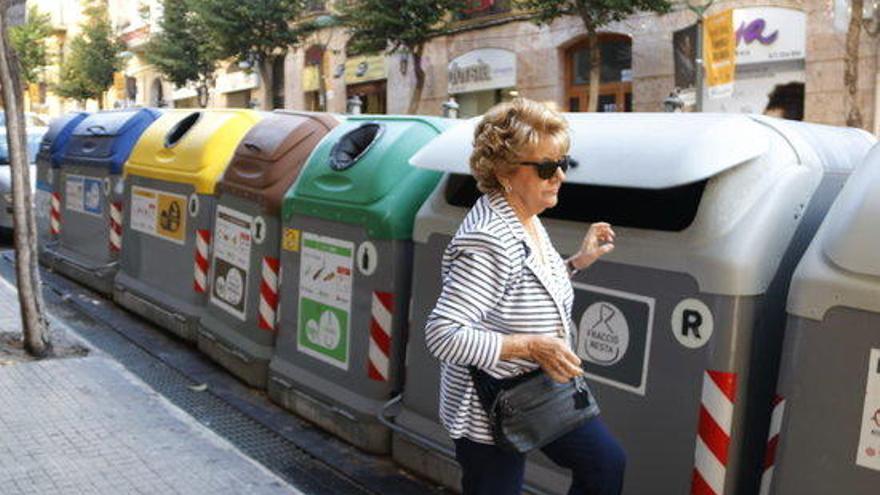 Una dona al costat de contenidors de reciclatge i brossa.