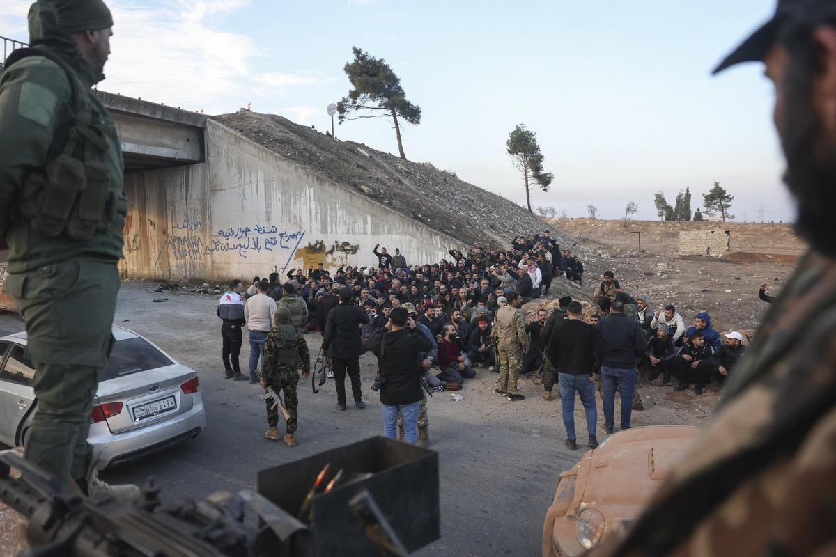 Soldados del gobierno y sus aliados se sientan en el suelo mientras son detenidos por los rebeldes en la carretera entre Homs y Damasco, cerca de Homs, Siria.