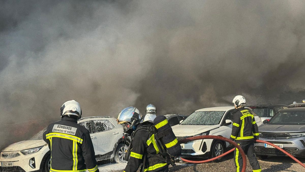 Efectivos de los bomberos tratan de sofocar un incendio que afecta a un aparcamiento con más de 100 vehículos aparcados