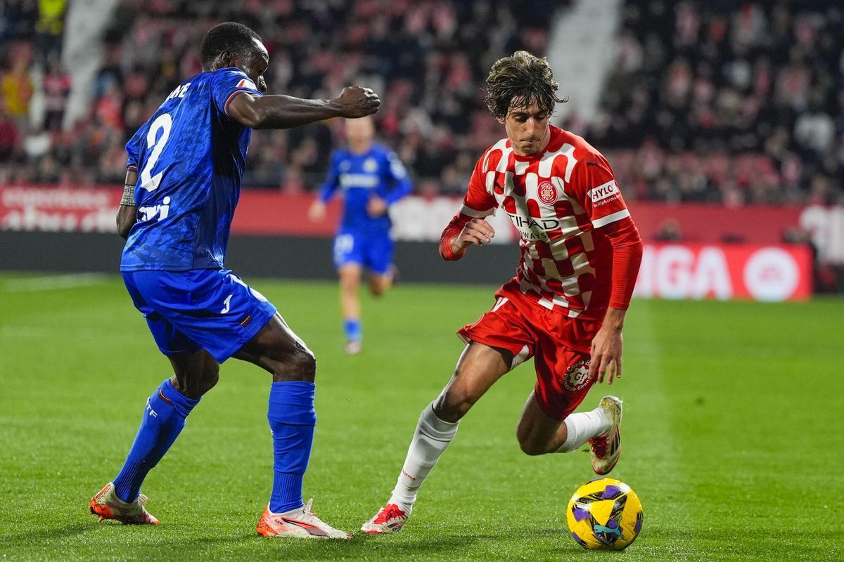 GIRONA, 14/02/2025.- El delantero del Girona, Bryan Gil (d), con el balón ante el defensa togolés del Getafe, Djene Dakoman, durante el encuentro correspondiente a la jornada 24 de Laliga EA Sports que disputan hoy viernes Girona y Getafe en el estadio de Montilivi, en Girona. EFE / Siu Wu.