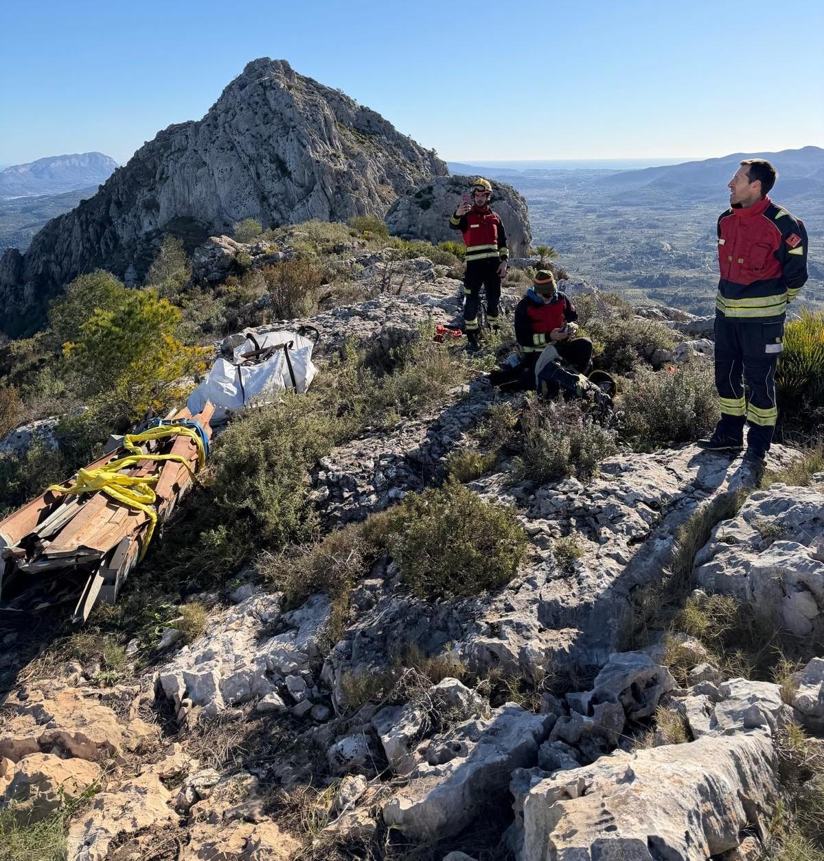 Los bomberos tras apilar los hierros cortados y meter en sacas los tornillos y baterías; al fondo, la cima del Cavall Verd y, a la izquierda, el perfil del Montgó