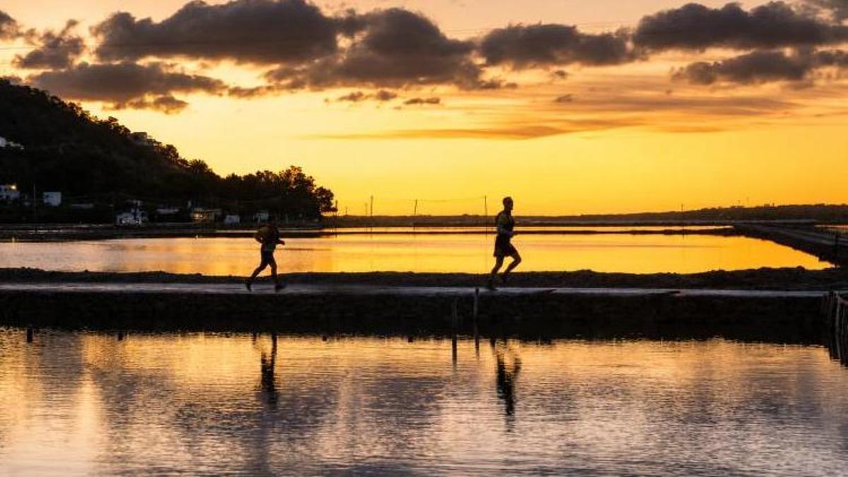Dos corredores atraviesan un camino en el 3 Días Trail Ibiza con el atarceder de fondo.