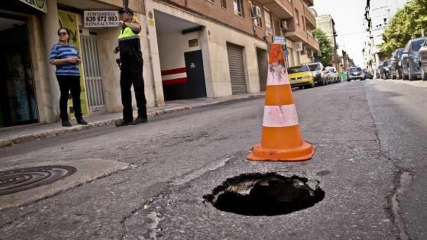 Un policía local conversa con una vecina junto al socavón aparecido en el centro de la calzada.