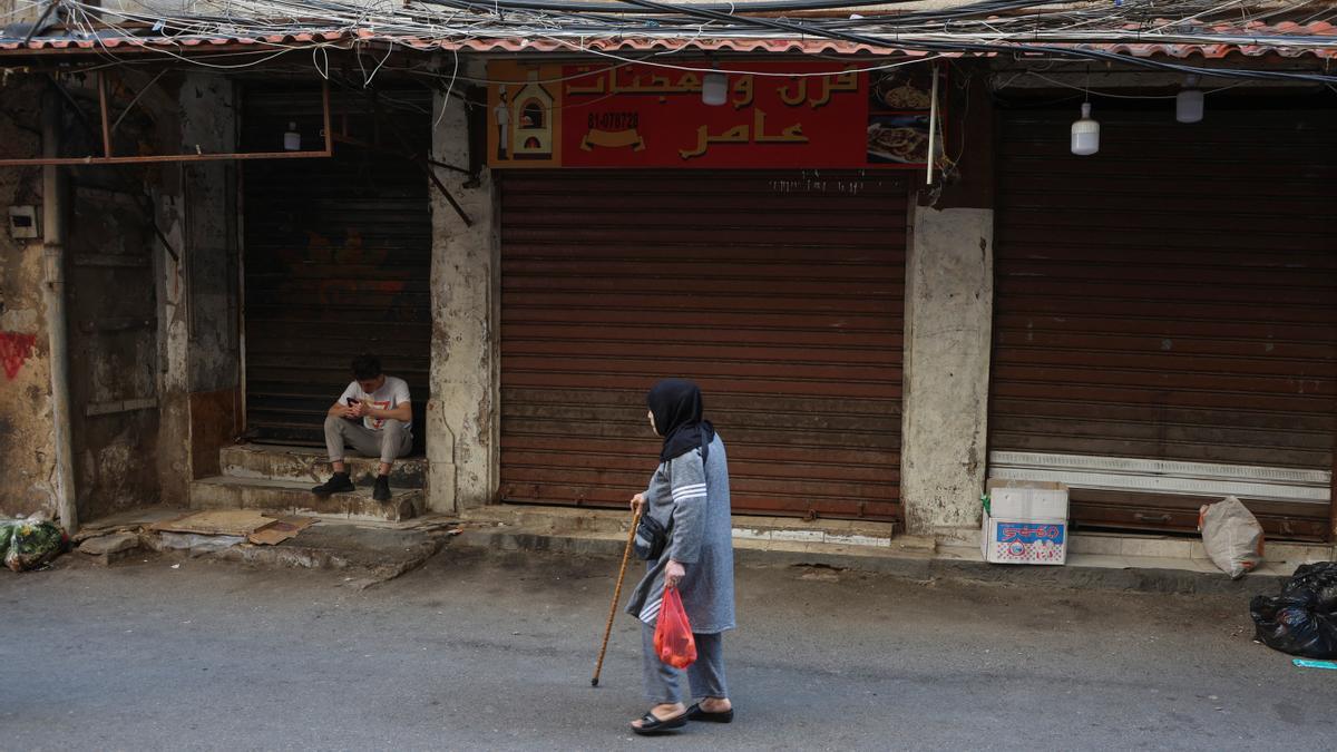 A woman walks past shops closed in response to the global call for a strike in solidarity with Gaza and Palestinian people, at Burj al-Barajneh refugee camp in Beirut