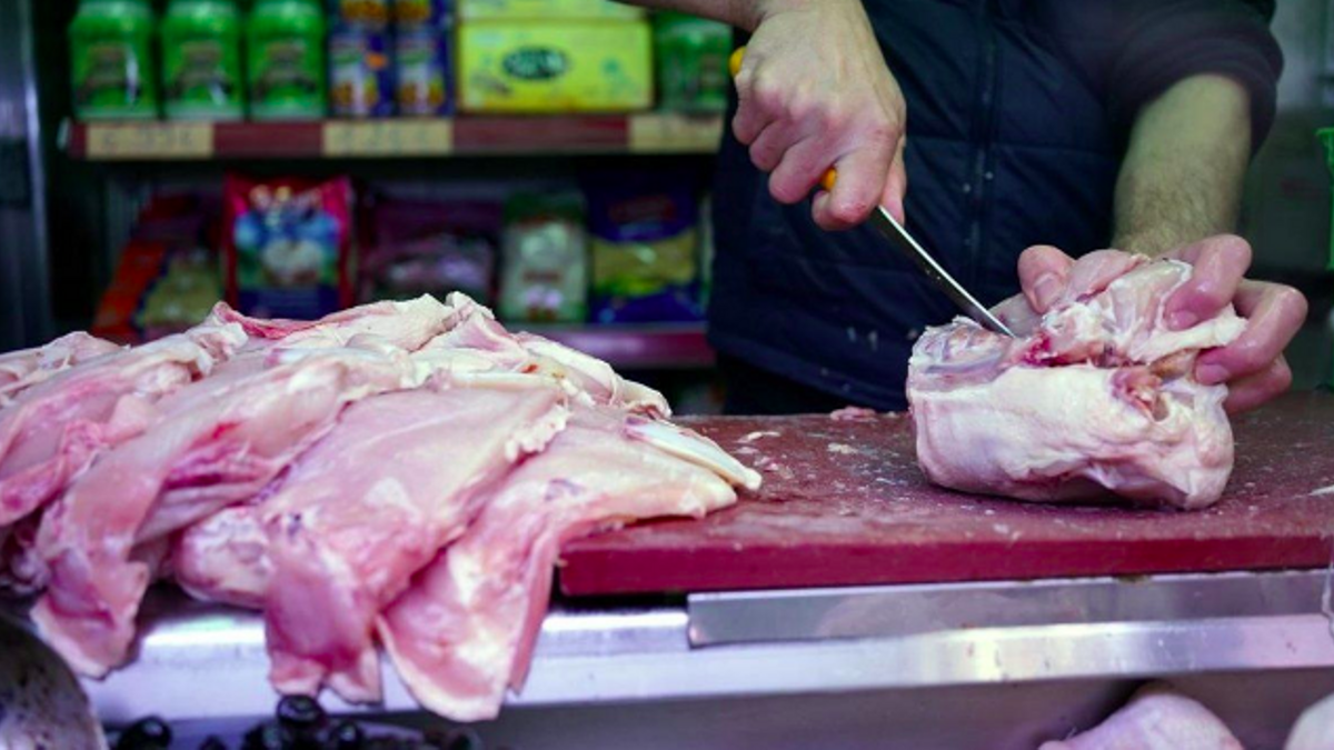 El dependiente de un mercado trocea un pollo para un cliente.