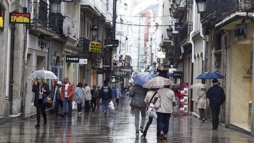 Viandantes con paraguas caminan por calle Real.