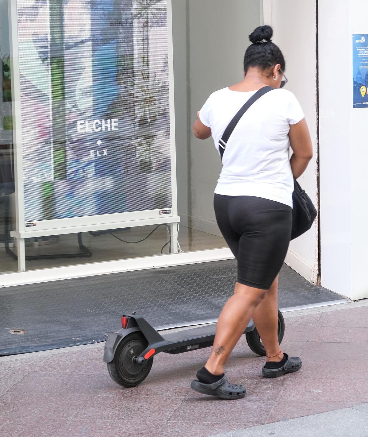 La dueña de un patinete camina por el centro de Elche a pie
