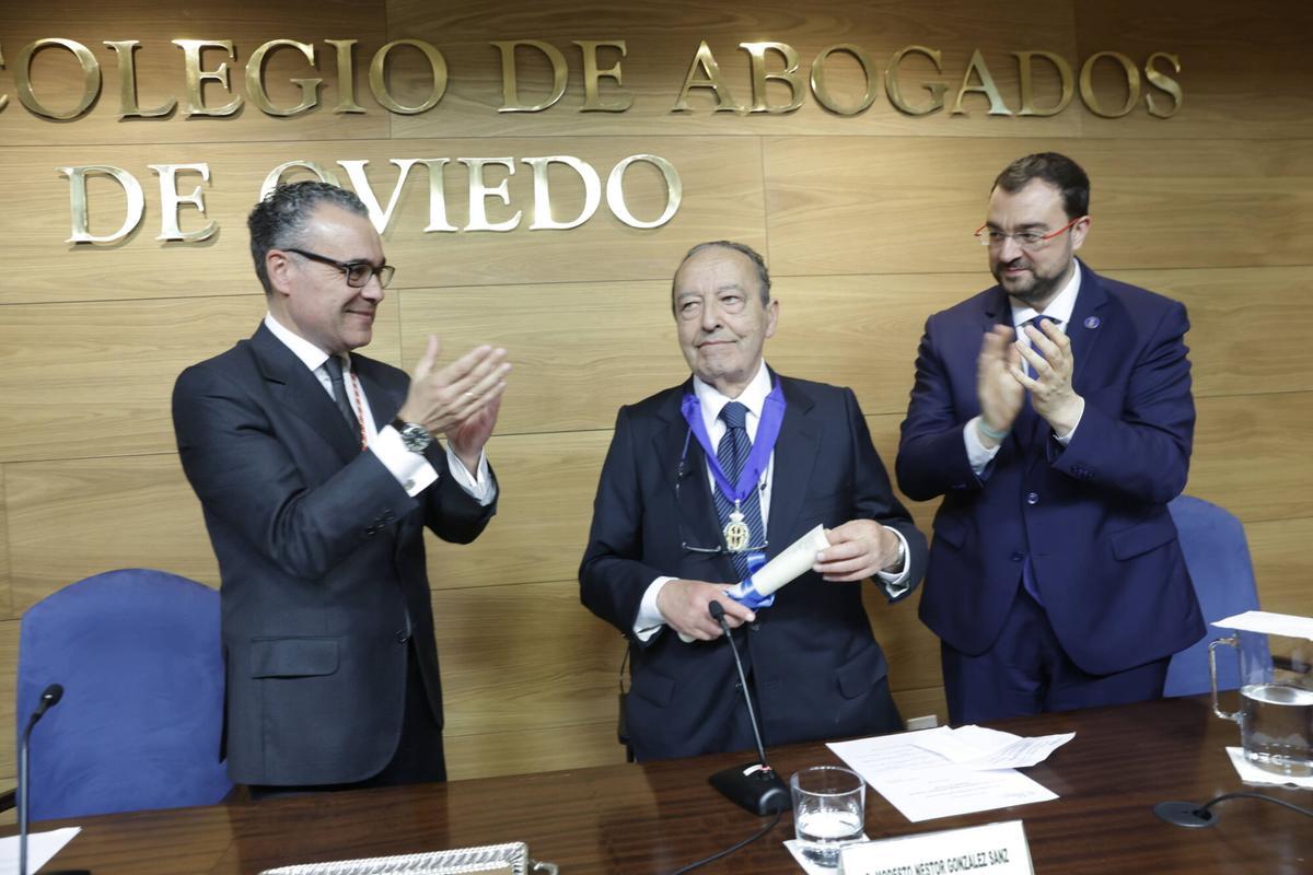 Modesto Néstor González, con la medalla del Colegio de Abogados y el título acreditativo en las manos, recibe el aplauso del decano, Antonio González-Busto, a la izquierda, y del presidente del Principado, Adrián Barbón.