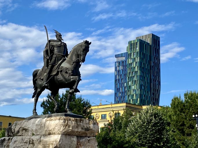 Estatua del héroe nacional de Albania con arquitectura moderna al fondo.