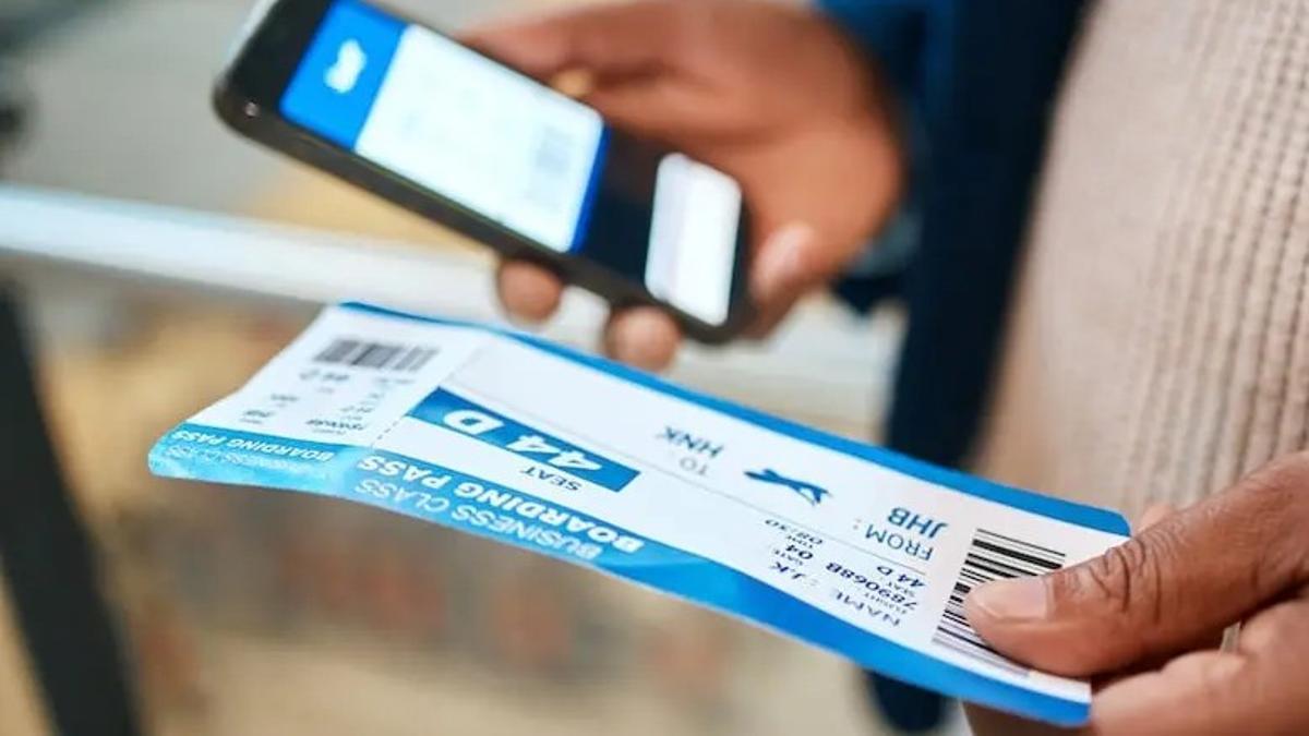 Una persona consulta los datos de su vuelo en el móvil mientras sostiene su tarjeta de embarque.