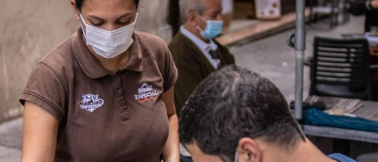 Una camarera sirve a un cliente, ambos con mascarilla, en un bar.