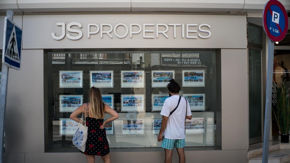 Dos personas observan inmuebles en alquiler y en venta en un escaparate de una inmobiliaria de Palma.