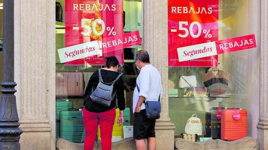 Una pareja observa los descuentos de segundas rebajas en un escaparate.