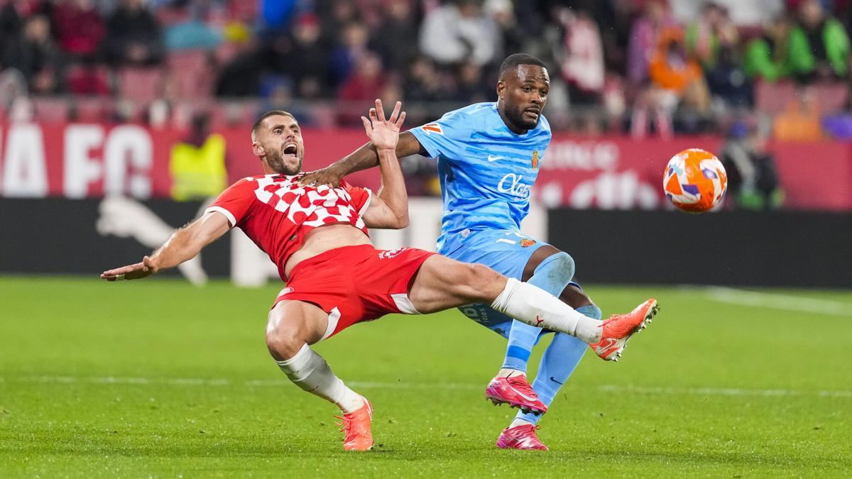 El defensa del Girona David López (i) cae ante Cyle Larin, del Mallorca, durante el partido de LaLiga de fútbol que Girona FC y Real Mallorca disputan este lunes en el estadio de Montilivi