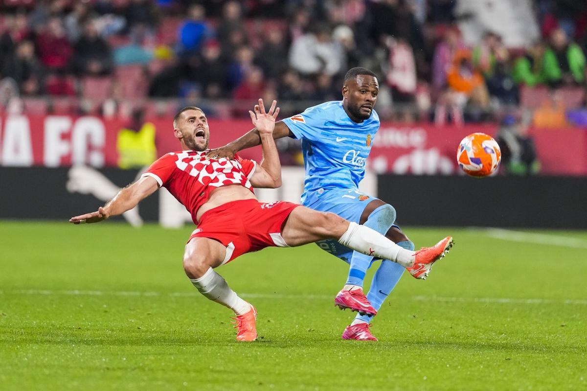El defensa del Girona David López (i) cae ante Cyle Larin, del Mallorca, durante el partido de LaLiga de fútbol que Girona FC y Real Mallorca disputan este lunes en el estadio de Montilivi