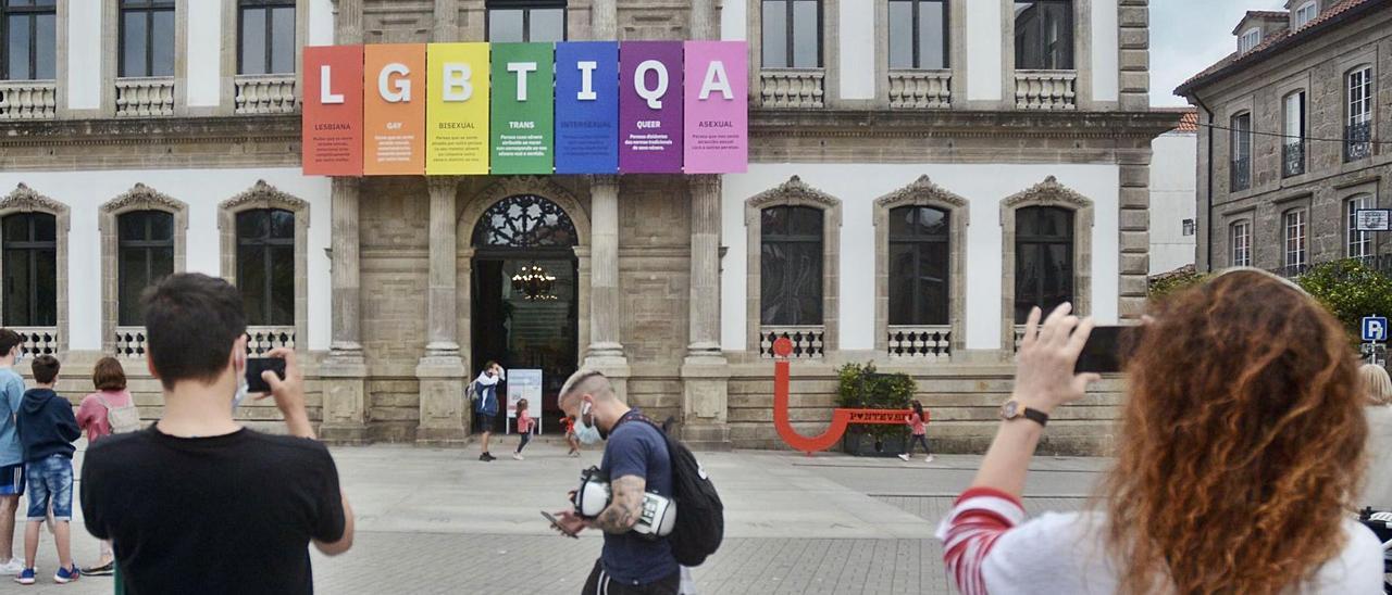 Varias personas se paran a fotografiar la bandera LGBTIQA que prende del balcón del Consistorio. |   // RAFA VÁZQUEZ