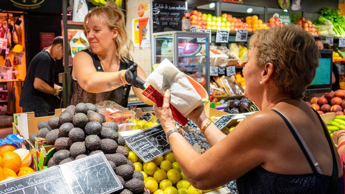 Una paradista atiende a una clienta en un comercio de fruta y verdura de un mercado de Barcelona