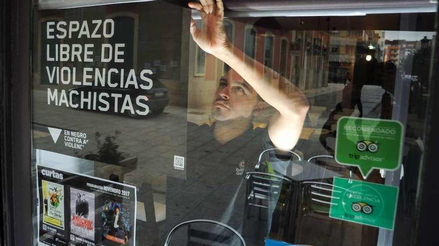 El responsable del bar Misterio, colocando un cartel contra la violencia hacia las mujeres.  // Iñaki Abella